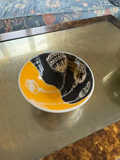 Ceramic bowl with a split black and yellow glaze featuring poppy seed pod illustrations.