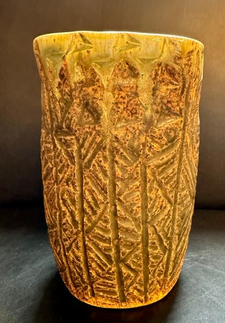Textured ceramic vase with vertical carvings in earthy tones and a pale green rim.