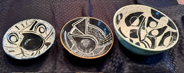 Three ceramic bowls featuring black and white abstract designs resting on a dark textured cloth.