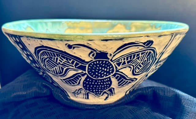 White ceramic bowl with a large dark blue sgraffito bee design and light green interior.