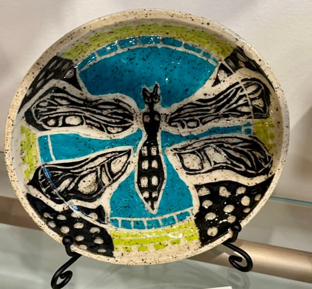 Speckled ceramic plate with a stylized black dragonfly design over turquoise and lime green glazes.