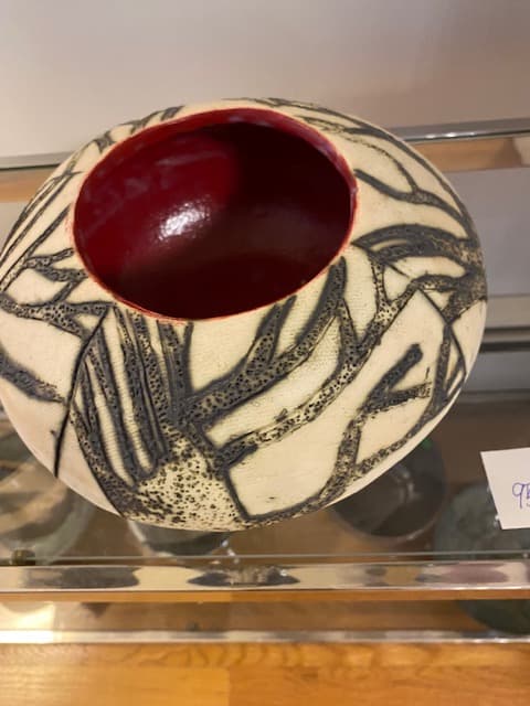 Round ceramic vessel with black abstract patterns on cream exterior and glossy red interior.