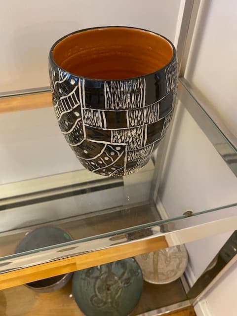 Black and white patterned ceramic vase with an orange interior on a glass shelf.