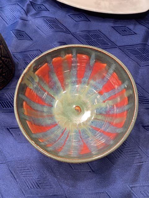 Ceramic bowl with orange interior and blue glaze drips on a blue patterned fabric background.
