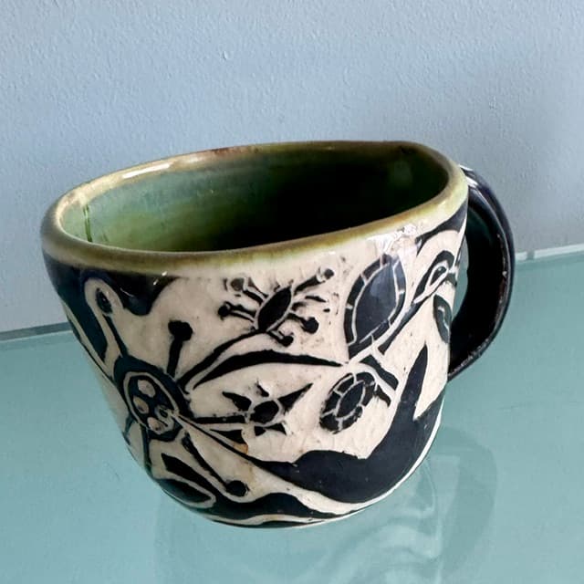 Handmade ceramic mug with green interior and black-and-white sgraffito designs of nature motifs.