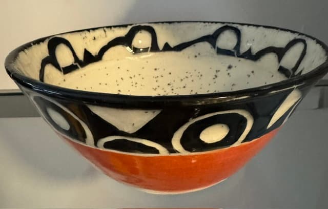 Ceramic bowl with an orange base, black and white abstract patterns, and a speckled interior.
