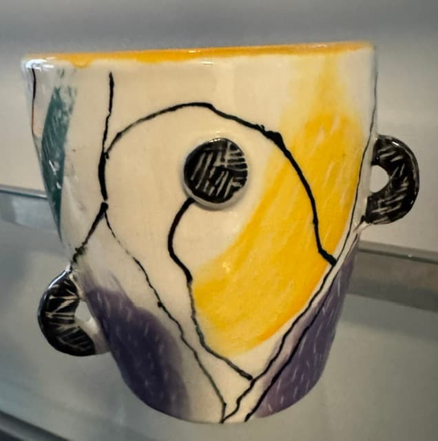 Abstract ceramic vessel with yellow and purple washes, black linework, and small textured handles.