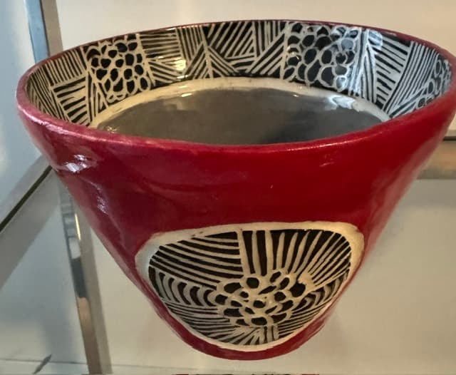 Red ceramic bowl with black and white geometric patterns on the interior rim and side.