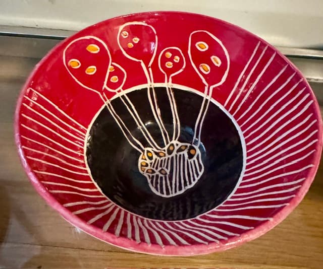 Red and black ceramic bowl featuring white hand-painted balloon designs and radiating white lines.