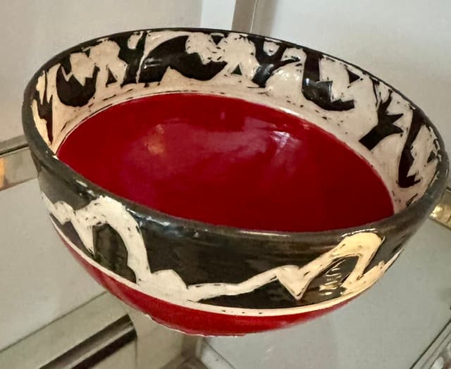 Ceramic bowl with a deep red interior and black and white abstract exterior patterns.