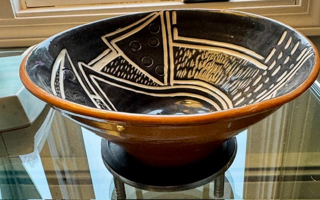 Handcrafted terracotta bowl with black interior and white geometric designs on a glass table.