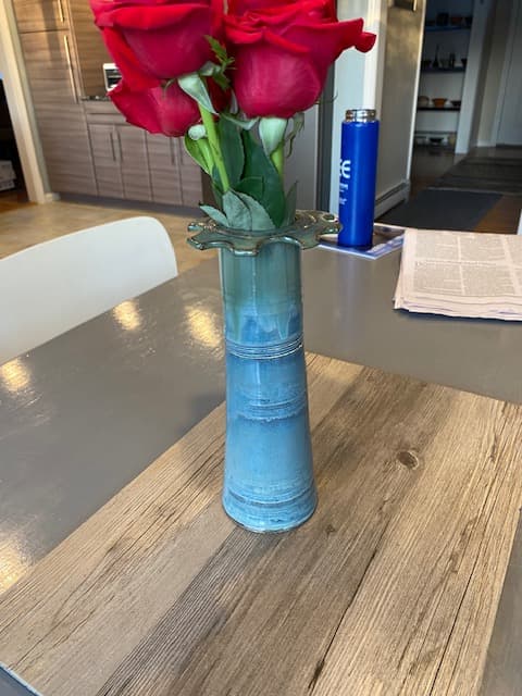 Vibrant red roses in a blue ceramic vase on a wooden table in a kitchen.