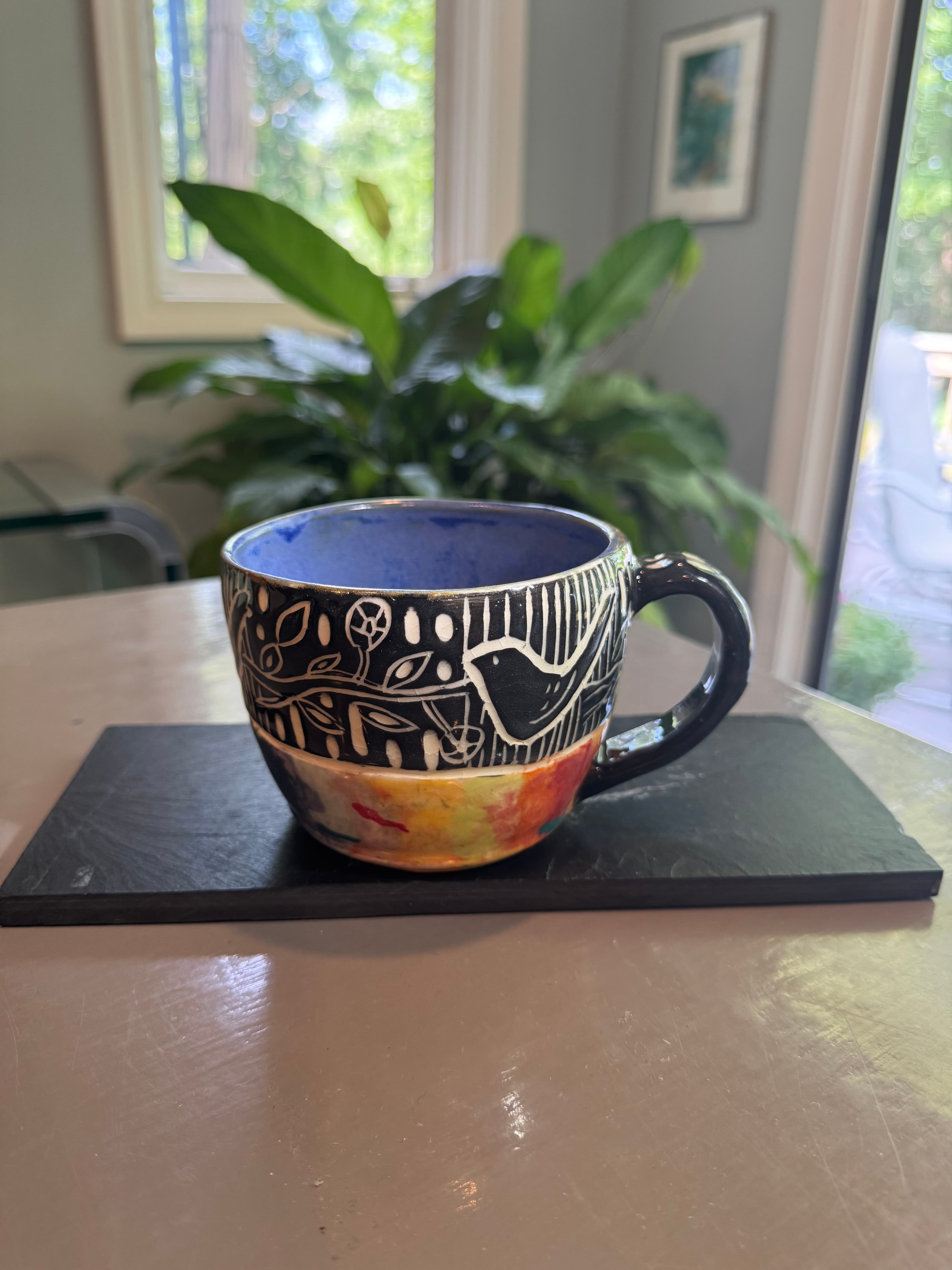 Hand-painted ceramic mug with a black sgraffito bird pattern and a colorful, abstract base.