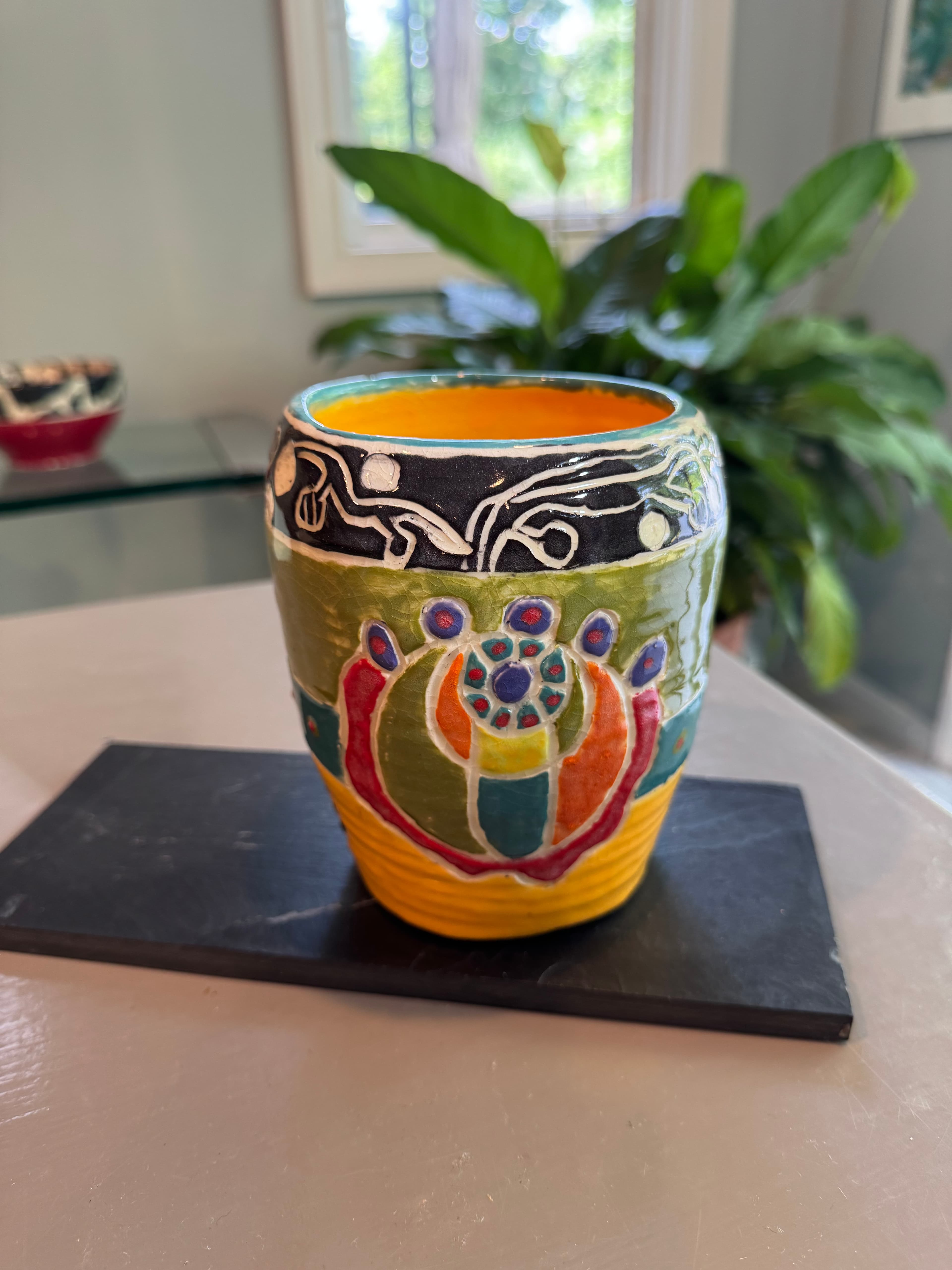 Vibrant ceramic cup with intricate colorful designs resting on a dark slate tile indoors.