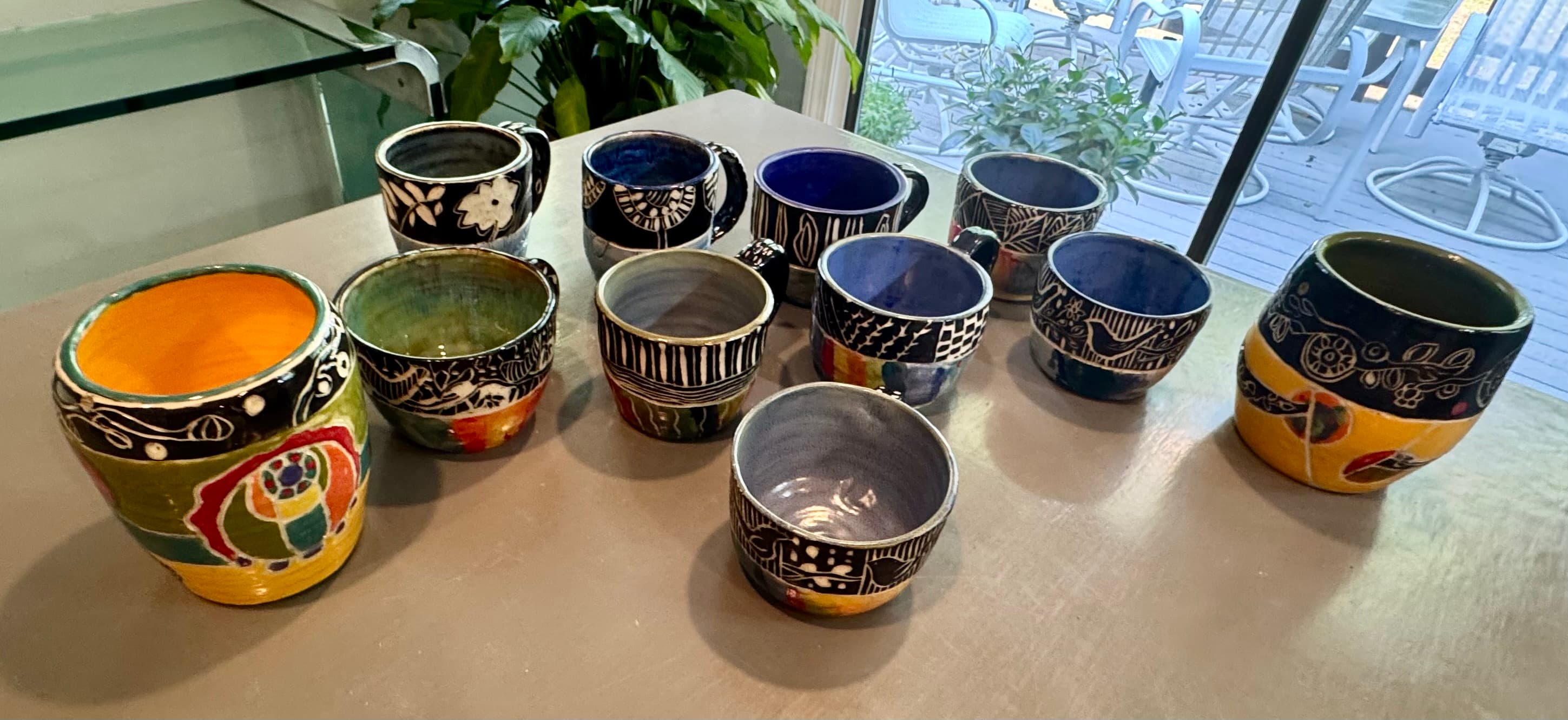 Handcrafted ceramic mugs and bowls featuring vibrant glazes and intricate black and white patterns.