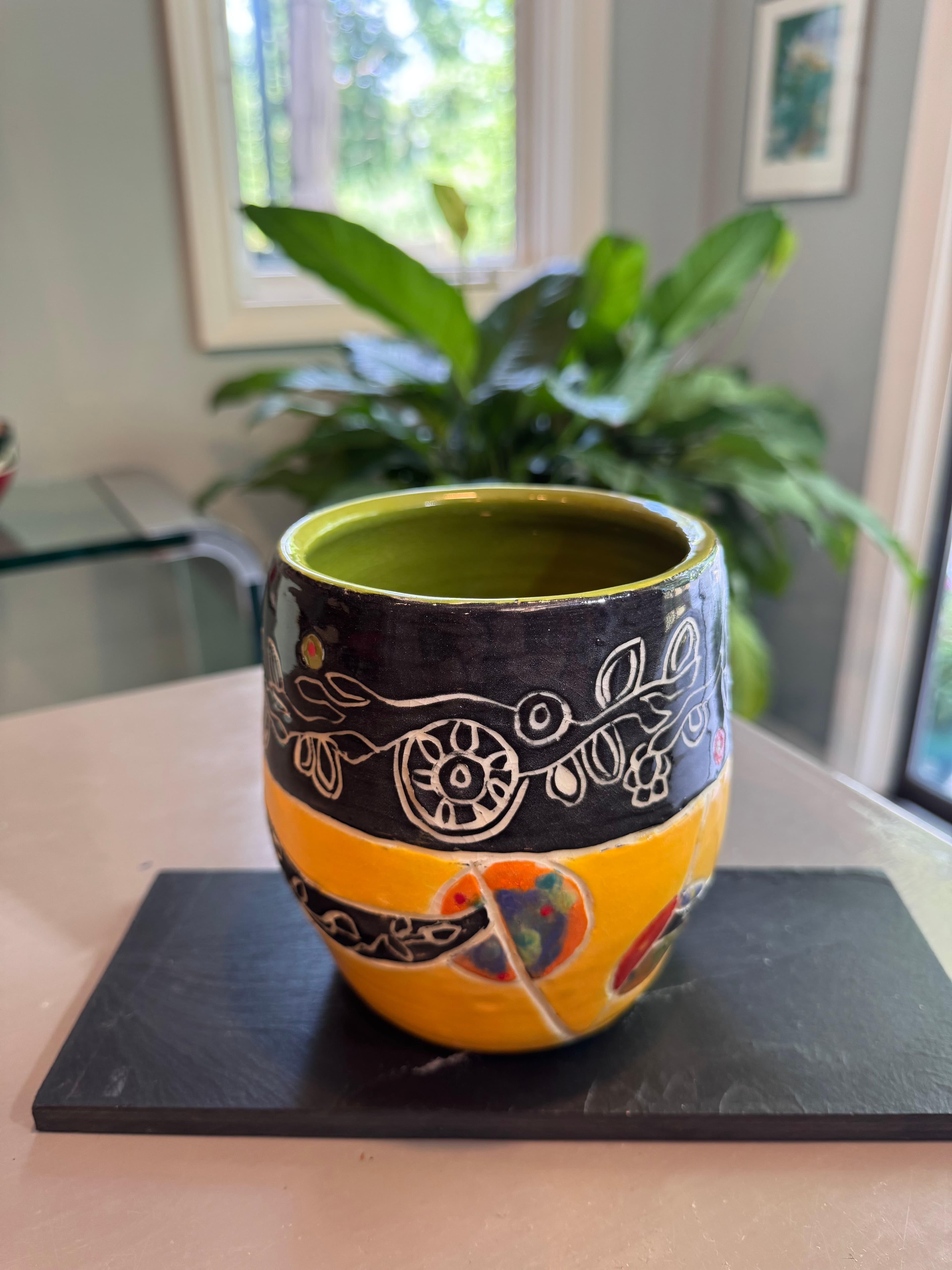 Decorative ceramic cup with black and yellow bands featuring intricate white floral line art.