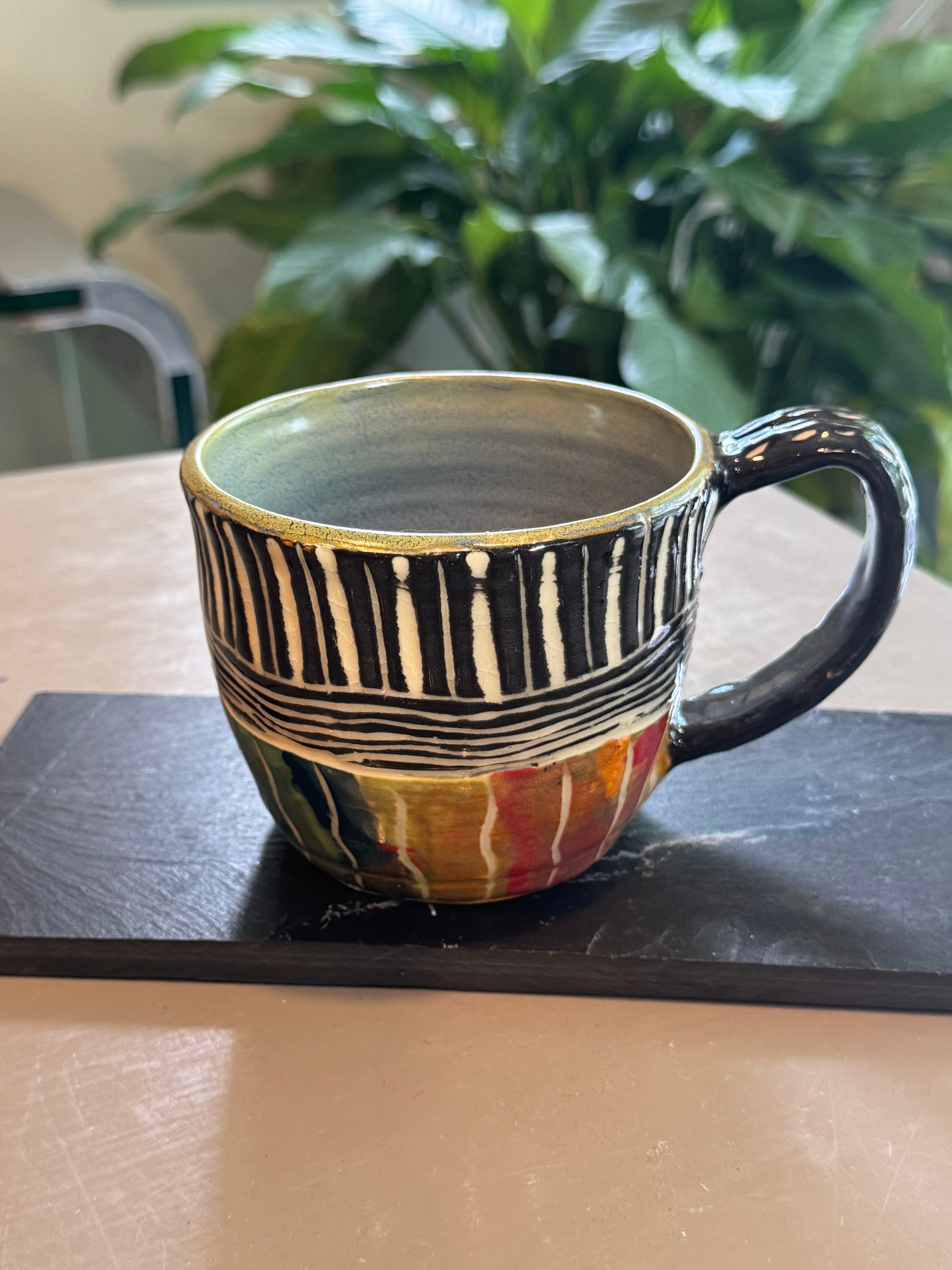 Hand-painted ceramic mug featuring black and white stripes and colorful abstract patterns on slate coaster.