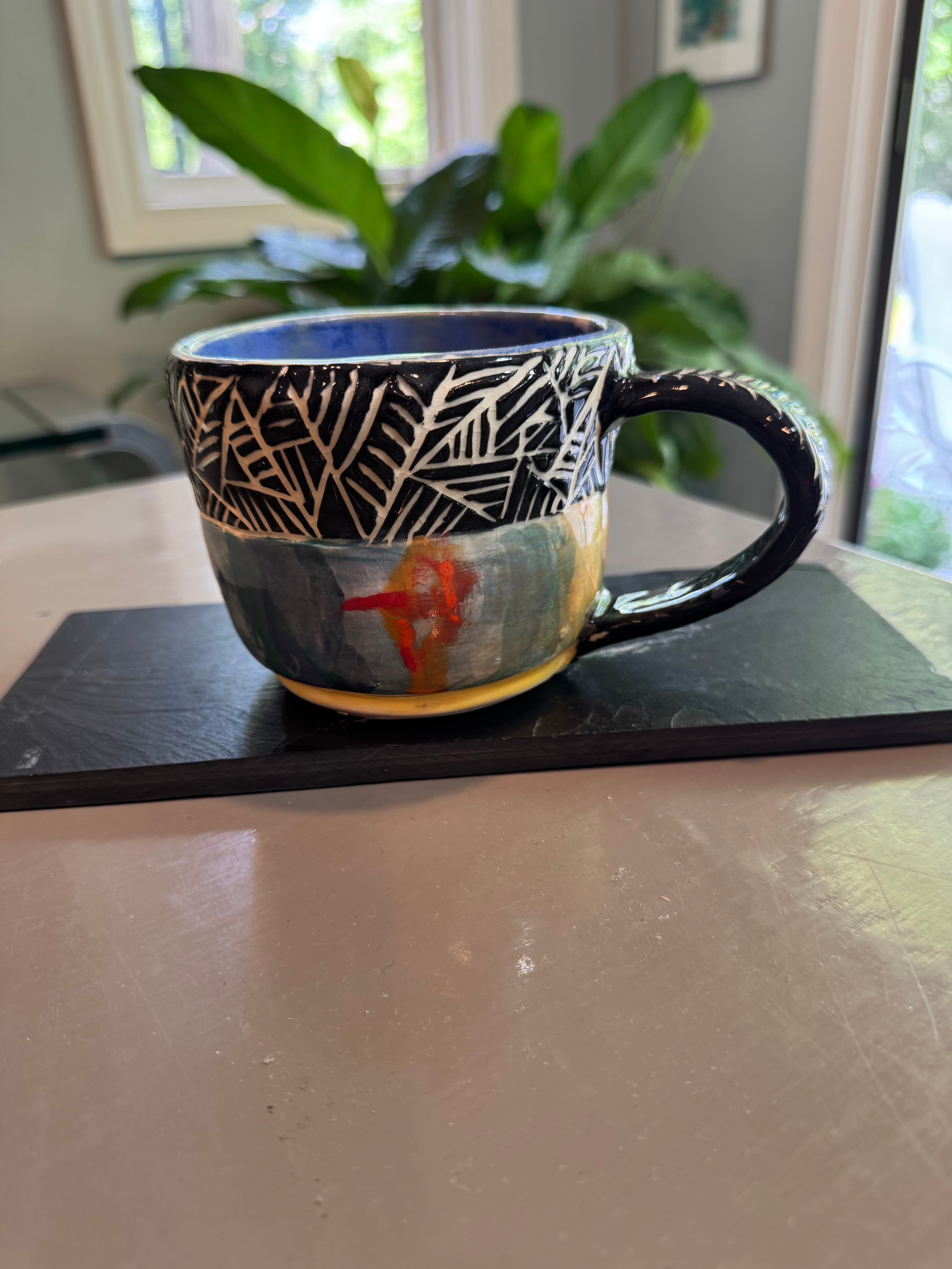 Handmade ceramic mug with black sgraffito patterns on top and colorful abstract glaze below.