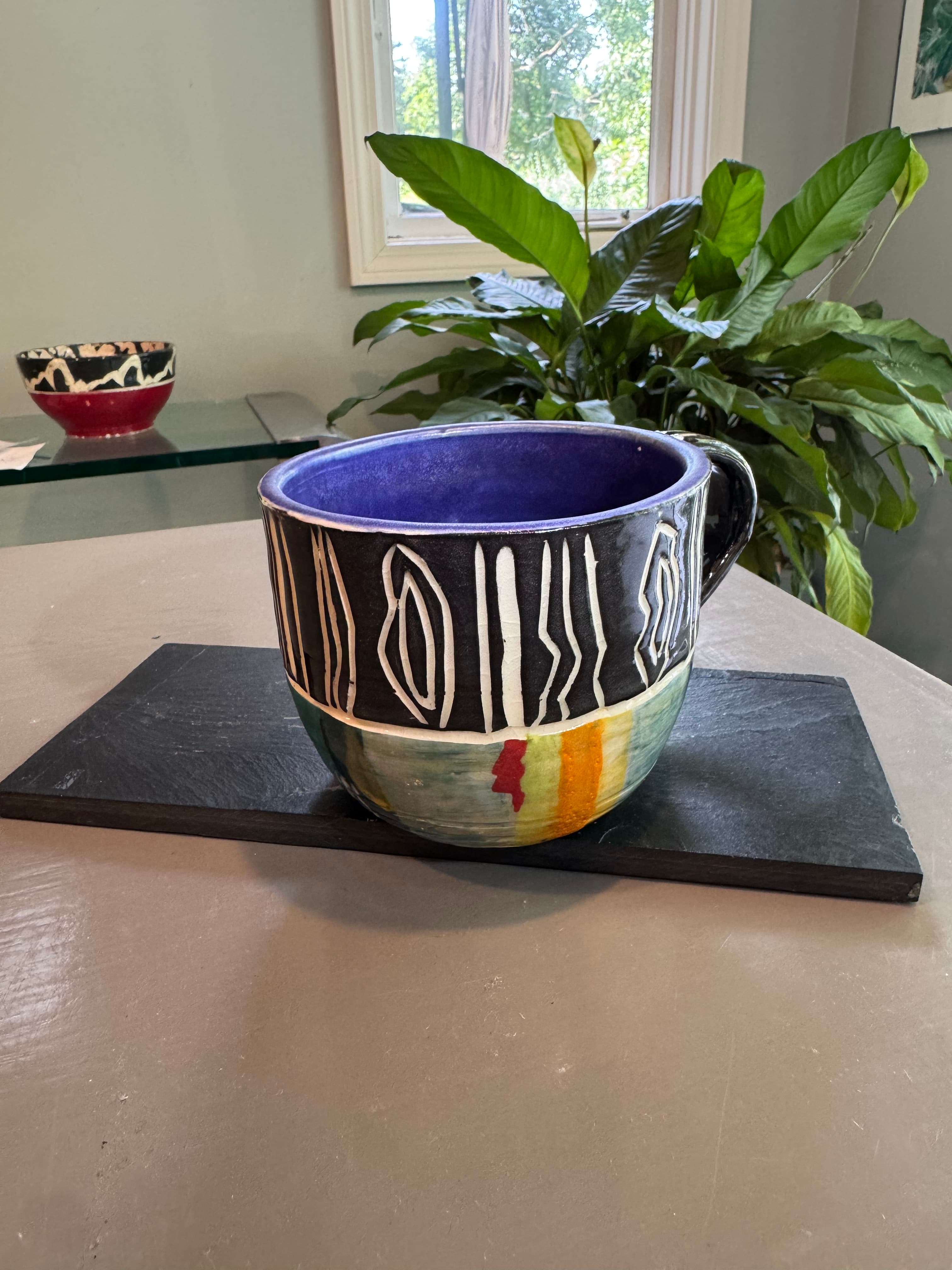 Hand-painted ceramic mug with purple interior and black-and-white abstract designs on a slate base.