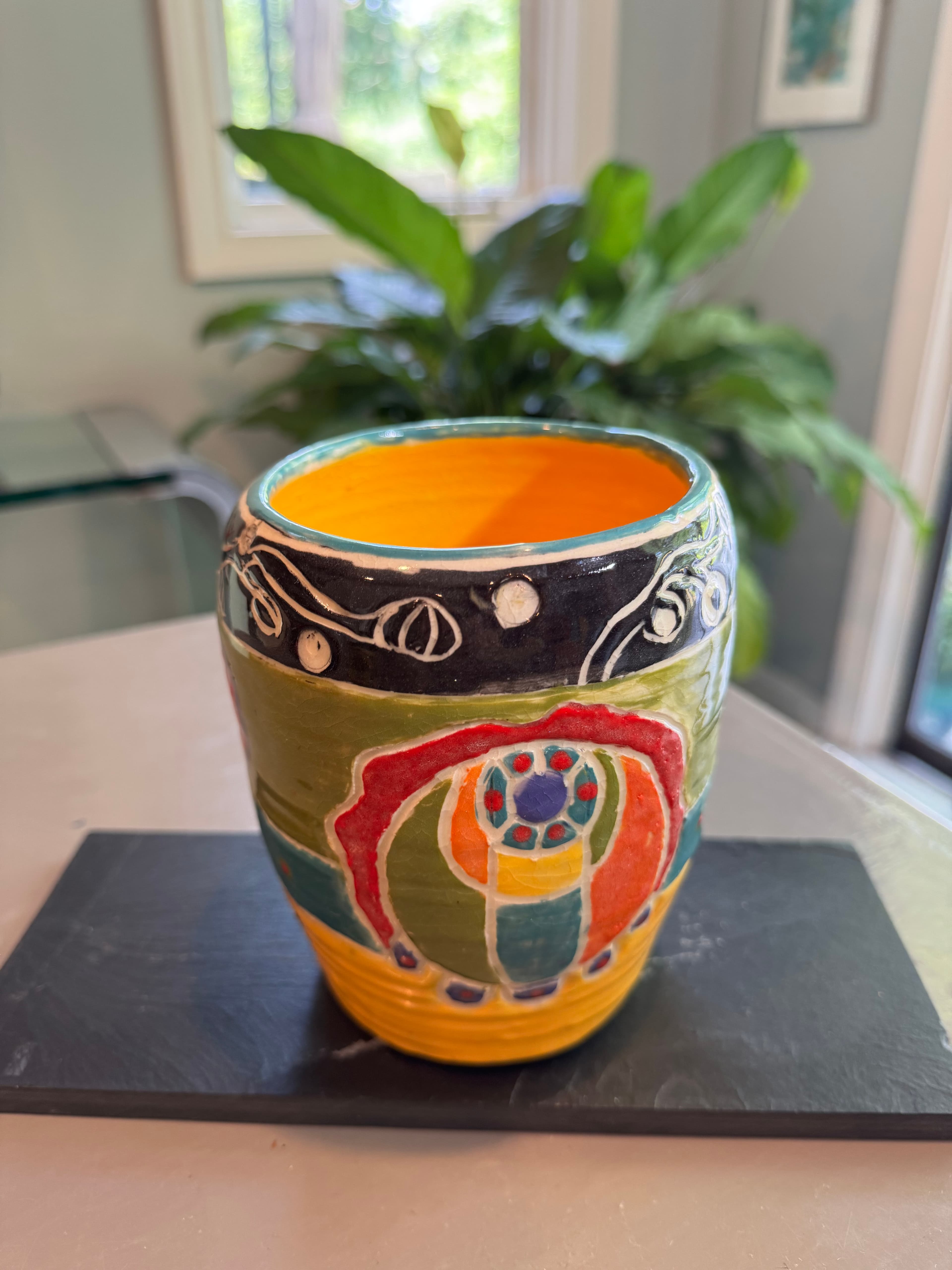 Hand-painted ceramic cup with vibrant abstract patterns resting on a black slate coaster.