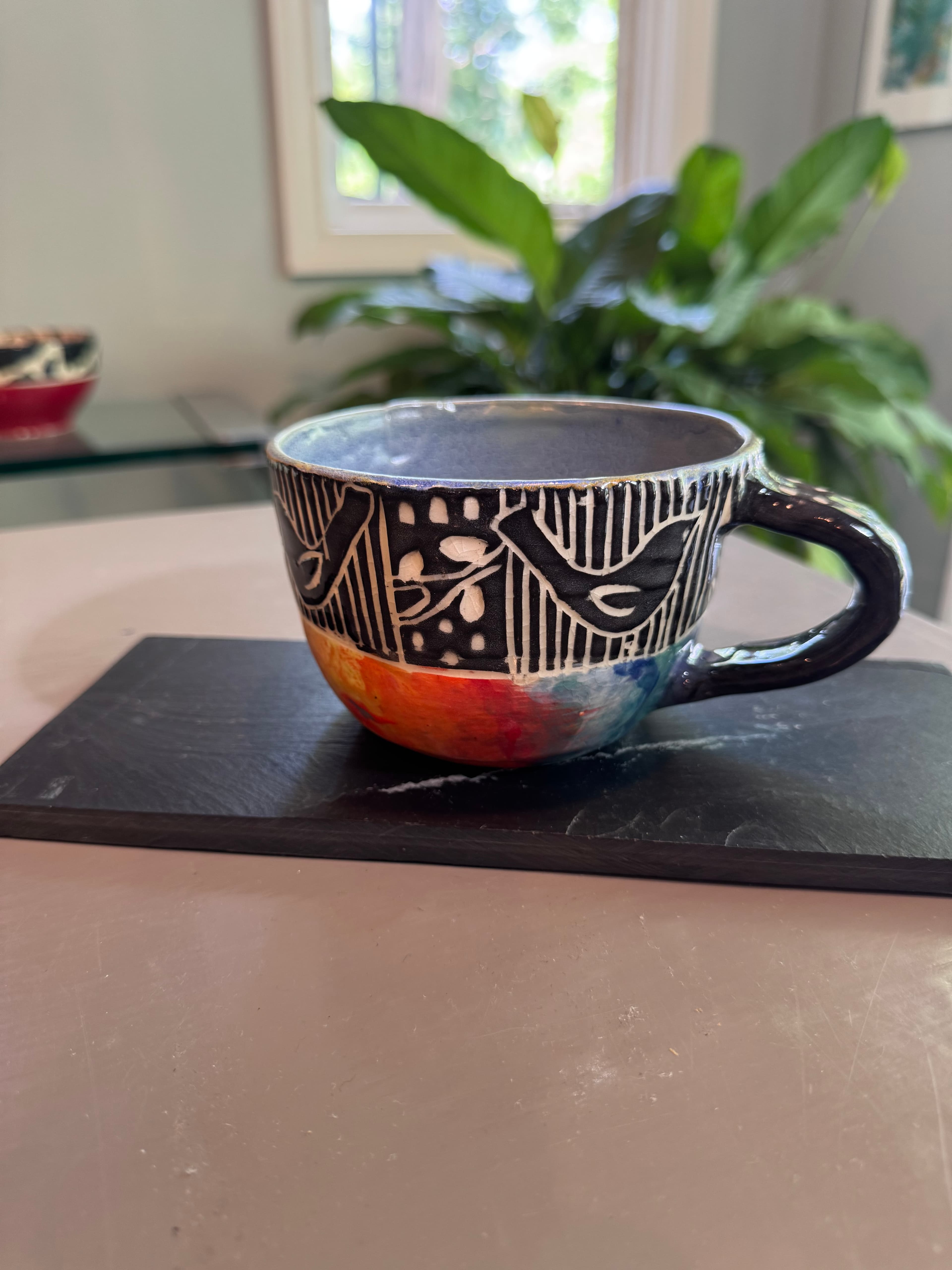 Handmade ceramic mug with black and white bird patterns and a colorful, painted base.